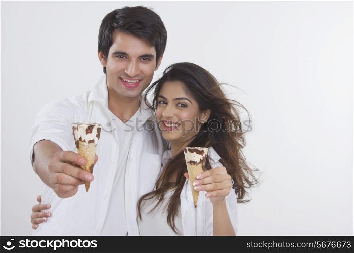 Portrait of loving young couple showing ice-cream cones over white background