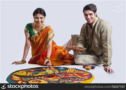 Portrait of Maharashtrian couple placing diyas on rangoli