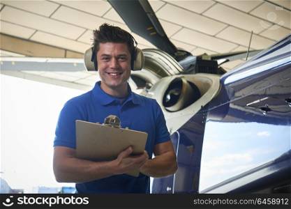 Portrait Of Male Aero Engineer With Clipboard Carrying Out Check On Helicopter In Hangar