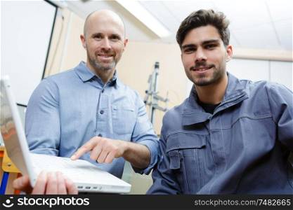 portrait of male apprentice with supervisor pointing at laptop