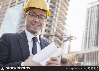Portrait of male architect on site carrying blueprints