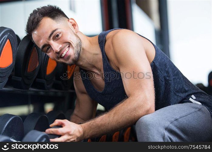 portrait of male bodybuilder sat by rack of weights