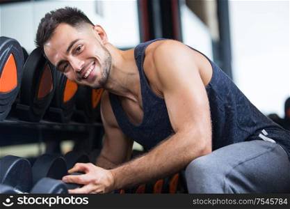 portrait of male bodybuilder sat by rack of weights