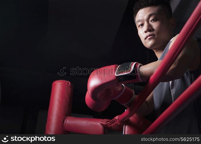 Portrait of male boxer resting his elbows on the ring side, looking at camera, low angle view