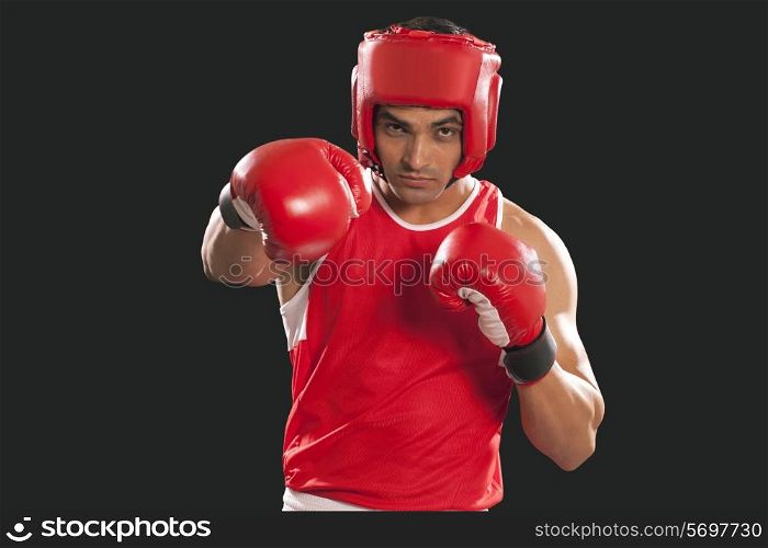 Portrait of male boxer wearing gloves and head protector against black background