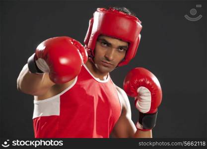 Portrait of male boxer wearing gloves and head protector as he punches the air isolated over black background