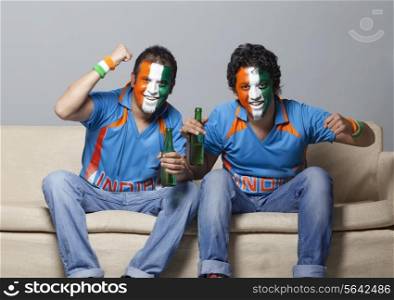 Portrait of male cricket fans with face painted in Indian tricolor cheering while having drink at home