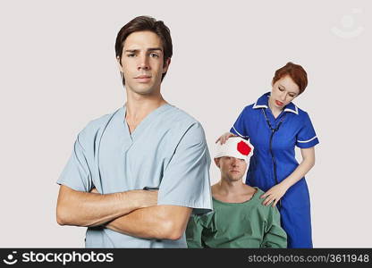 Portrait of male doctor with female nurse treating an injured patient against gray background