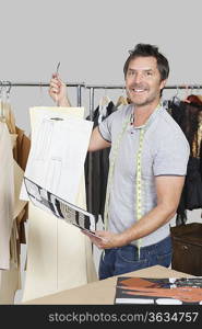 Portrait of male dressmaker holding sewing pattern, sketch and design draft