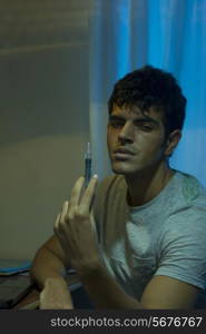 Portrait of male drug addict holding syringe at home