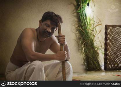 Portrait of male farmer sitting indoors holding stick