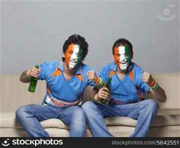 Portrait of male friends on sofa with painted face cheering while having drink at home