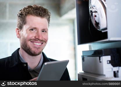 Portrait Of Male Heating Engineer Working On Central Heating Boiler Using Digital Tablet