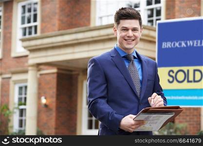 Portrait Of Male Realtor Standing Outside Residential Property With Sold Sign