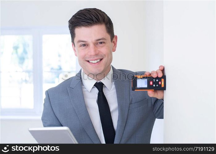 Portrait Of Male Realtor With Digital Tablet Measuring Room With Laser Measure