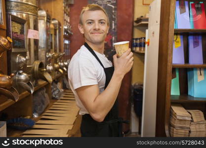 Portrait of male salesperson holding disposable coffee cup in store