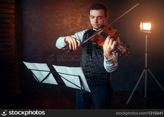 Portrait of male violinist with violin against music stand. Fiddler man with musical instrument playing in studio, solo concert training