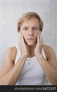 Portrait of man applying aftershave moisturizer in bathroom