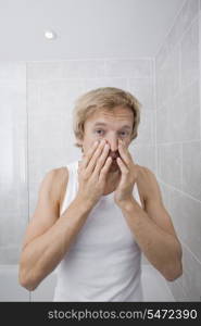 Portrait of man checking for wrinkles on his face in bathroom