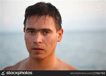 Portrait of man come up from water, on background of the sea and sky. Looks in camera.