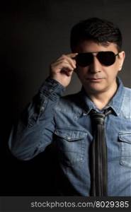 Portrait of man in Blue jean shirt and and black tie with sunglasses on black background