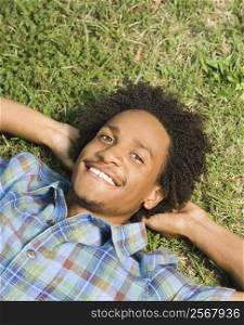 Portrait of man lying in grass smiling with hands behind head.