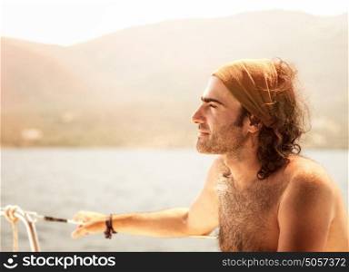 Portrait of man sitting on sail boat and enjoying mild sunset light, handsome captain of luxury water transport, summer vacation concept