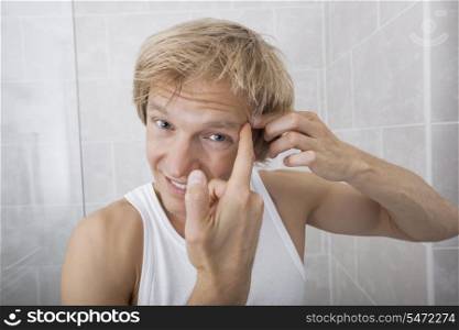 Portrait of man squeezing pimple on his forehead in bathroom