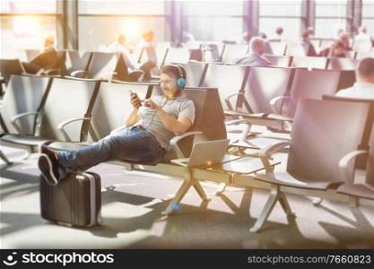 Portrait of man using smartphone with headphones on while waiting for boarding in airport