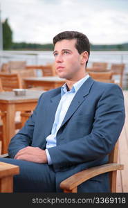 Portrait of man, who sits behind table in cafe near water