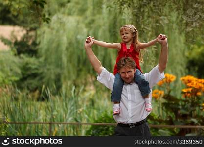 Portrait of man with a daughter in summer garden. Girl sits at father on shoulders.