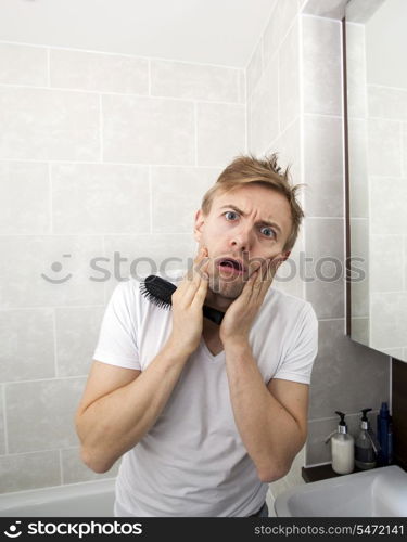 Portrait of man with hairbrush grimacing in bathroom