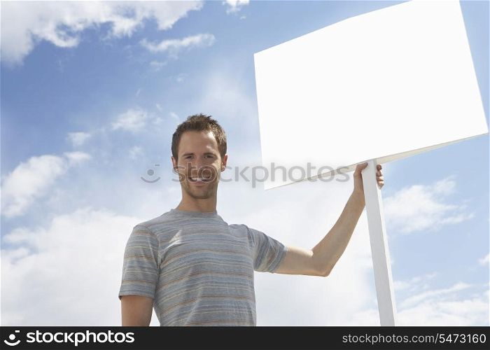 Portrait of man with standing by blank sign against cloudy sky