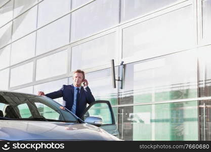 Portrait of mature attractive businessman talking on smartphone while standing outside the car