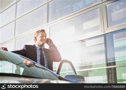 Portrait of mature attractive businessman talking on smartphone while standing outside the car