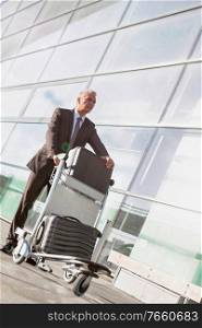 Portrait of mature businessman pushing luggage cart with his suitcase in airport