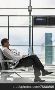 Portrait of mature businessman working on his laptop while sitting and waiting for flight in airport