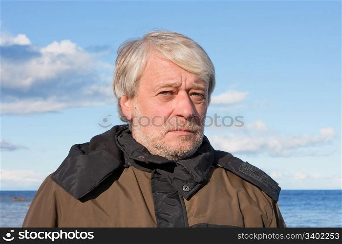 Portrait of mature concerned man with grey hair at the Baltic sea in autumn day.