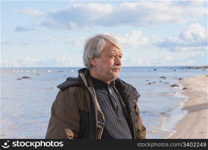 Portrait of mature concerned poor man with grey hair at the Baltic sea in autumn day.