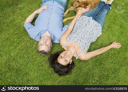 Portrait of mature couple lying on grass with dog