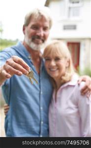 Portrait Of Mature Couple Standing In Garden In Front Of Dream Home In Countryside Holding Keys