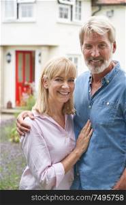 Portrait Of Mature Couple Standing In Garden In Front Of Dream Home In Countryside