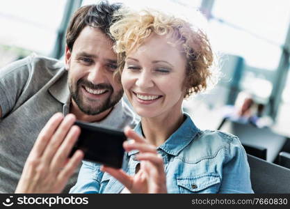 Portrait of mature couple taking and looking at their selfie while waiting for boarding in airport