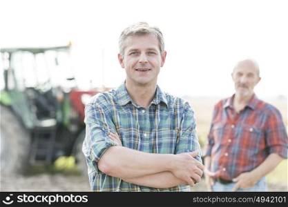 Portrait of mature farmer with arms crossed against coworker at farm