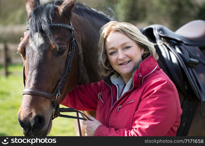 Portrait Of Mature Female Owner In Field With Horse