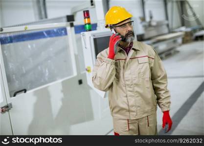Portrait of mature industrial man engineer with smartphone in a factory