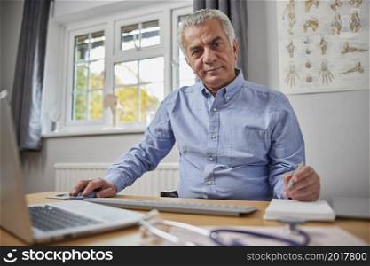 Portrait Of Mature Male GP At Desk In Doctors Office