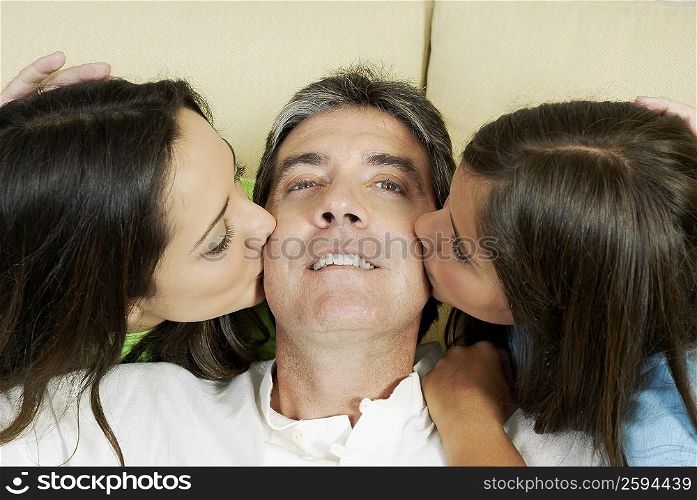 Portrait of mature man being kissed by his two daughters
