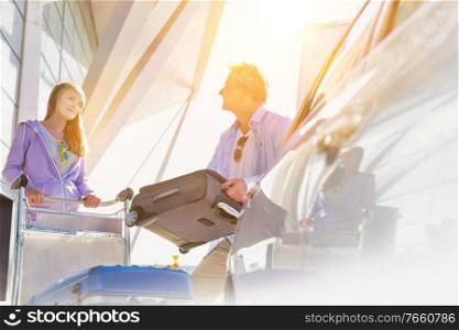 Portrait of mature man putting luggage on car trunk with lens flare