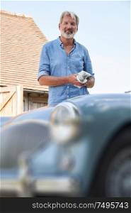 Portrait Of Mature Man Restoring Classic Sports Car Outdoors At Home